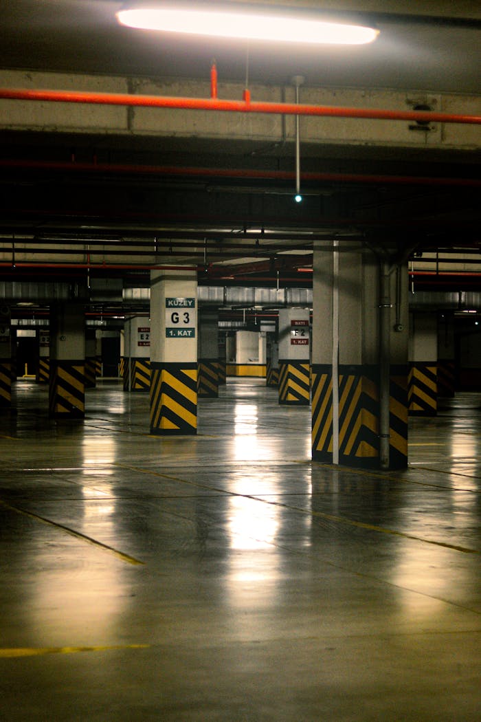Empty underground parking lot with striped poles and reflective floor lighting.