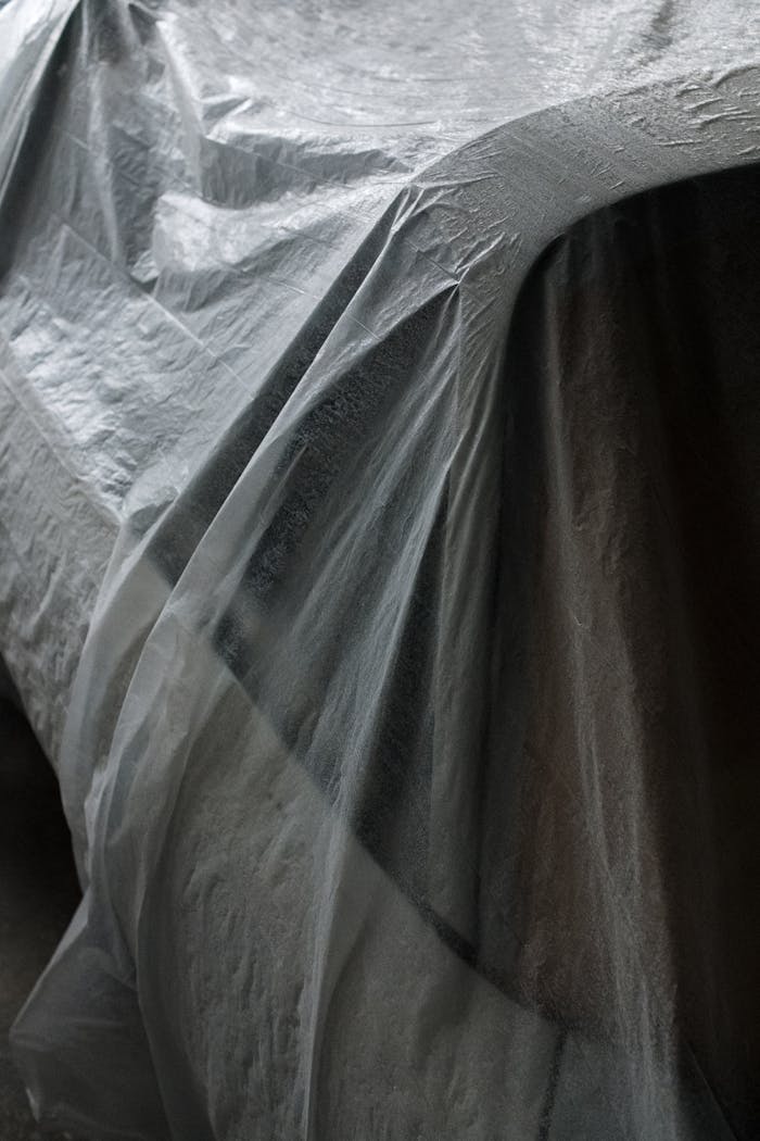 A classic car covered with a plastic sheet in a garage setting, emphasized on vintage preservation.